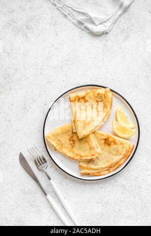 Pfannkuchen mit Zitronen auf weißem Hintergrund, Ansicht von oben, kopieren. Hausgemachte dünne Crepes auf dem Teller zum Frühstück oder Dessert. Stockfoto