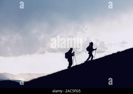 Zwei Wanderer Silhouetten geht zusammen bergauf in den Bergen gegen Wolken Stockfoto