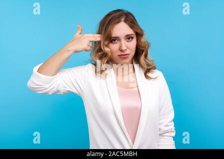 Portrait von frustrierten Frau mit gewelltes Haar in weisse Jacke Zeigefinger Pistole mit gelangweilten Gesichtsausdruck, die sich in Depression, Ti Stockfoto