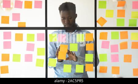 Afrikanische amerikanische junge Manager Hinzufügen von Aufgaben auf Glas Wand konzentriert. Stockfoto