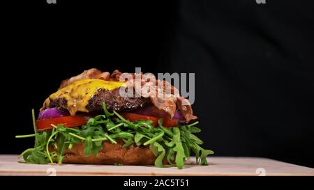 Handwerk Burger ist Kochen auf schwarzem Hintergrund. Bestehen: sauce, Rucola, Tomaten, roten Zwiebeln, Speck, rote Johannisbeeren Sauce, ricotta Cottage frischen Käse, Luft b Stockfoto