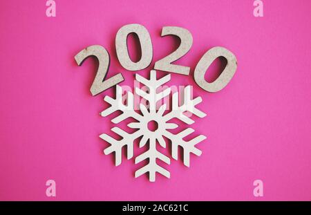 Minimalistischer flach Hintergrund mit 2020 Figuren und Holz- Schneeflocke Schuß von oben auf hell rosa Hintergrund. Frohes Neues Jahr Tapete mit Hand mad Stockfoto