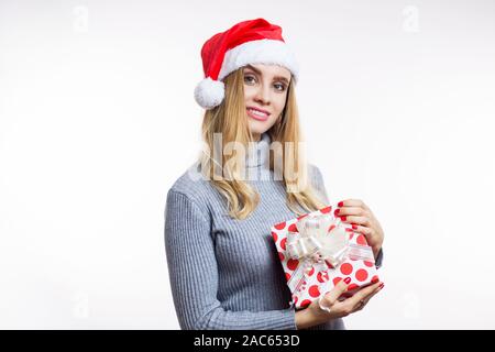 Weihnachten Porträt einer schönen blonden Frau in Rot Santa's Hut und Holding boxen mit einem Geschenk auf einem weißen Hintergrund. Urlaub, Feiern, neues Jahr Stockfoto