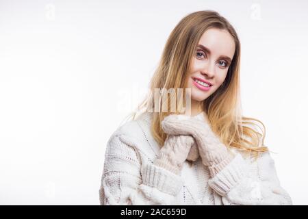 Gerne blonde Frau tragen beige Pullover, gestrickte Handschuhe und lächelnd an der Kamera auf weißem Hintergrund isoliert mit kopieren. Winter, Weihnachten, gemütliche Stockfoto