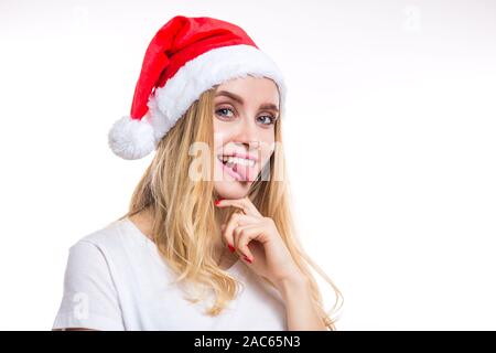 Lustig heiter lächelnd blonde Frau trägt eine rote Weihnachtsmütze und zeigt ihre Zunge an der Kamera auf einen weißen Hintergrund mit kopieren. Weihnachten, Silvester, ja Stockfoto