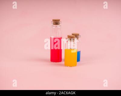 Blumen und Pflanzenextrakte oder Parfüm in kleinen Flaschen auf rosa Hintergrund. Drei kleine Blasen mit rot blau und gelb Flüssigkeit, das Konzept der Stockfoto