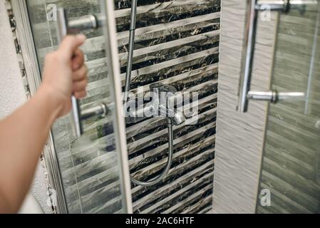 Eine Hand, öffnet die Tür zu den grauen Duschkabine. Es gibt kein Wasser aus dem Wasserhahn. Stockfoto