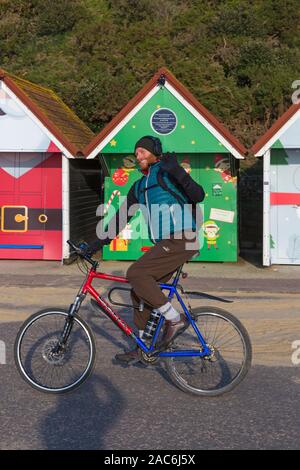 Bournemouth, Dorset UK. 1. Dezember 2019. Strand Hütten erhalten ihre Mäntel an Weihnachten am Strand von Bournemouth, als Santa und Elf auf einer trockenen, sonnigen Tag eingerichtet, aber bitter kalt. Radfahrer Fahrten entlang der Promenade vorbei an den Weihnachten Strandhütten. Credit: Carolyn Jenkins/Alamy leben Nachrichten Stockfoto
