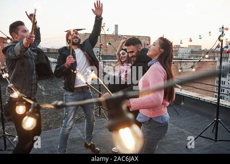 Schöne Menschen. Spielen mit Wunderkerzen auf dem Dach. Gruppe der jungen schönen Freunde Stockfoto