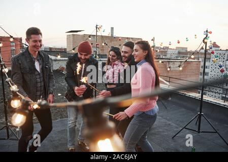 Gerne wieder Kind. Spielen mit Wunderkerzen auf dem Dach. Gruppe der jungen schönen Freunde Stockfoto