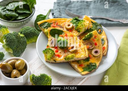 Omelette mit Brokkoli, Spinat und Oliven auf einem Teller. Frittata - italienisches Omelett mit grünem Gemüse. Stockfoto