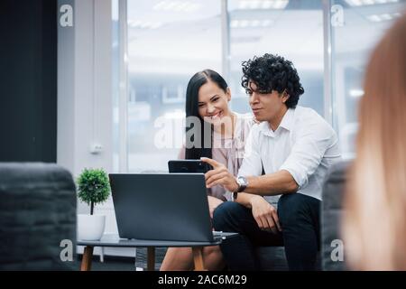 Haves eine Pause. Selfie von zwei lächelnde Büroangestellte in offizielle Kleidung, die sitzt in der Nähe von Silver Laptop am Tisch Stockfoto