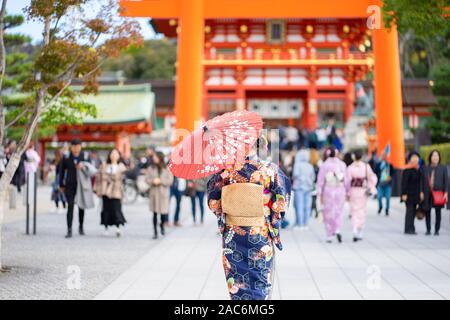 Geishas Mädchen mit japanischen kimono unter roten Holz- Tori Gate bei Fushimi Inari Schrein in Kyoto, Kimono ist ein traditionelles japanisches Gewand. Das Wort " Stockfoto