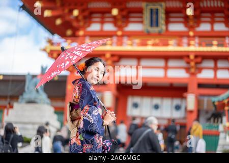 Geishas Mädchen mit japanischen kimono unter roten Holz- Tori Gate bei Fushimi Inari Schrein in Kyoto, Kimono ist ein traditionelles japanisches Gewand. Das Wort " Stockfoto