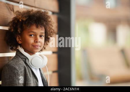 Portrait von afrikanischen Jungen mit lockigem Haar und mit Kopfhörern bei Kamera schaut beim Stehen im Freien Stockfoto