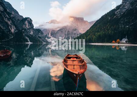 Sieht aus wie die Sonne untergeht. Boote aus Holz auf dem Crystal Lake mit majestätischen Berg hinter. Spiegelbild im Wasser. Kapelle befindet sich auf der rechten Küste Stockfoto