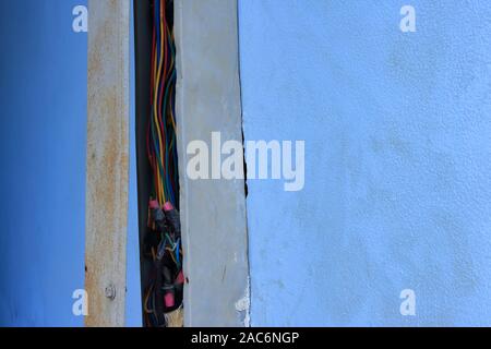Closeup freiliegende Stromleitungen in gebrochenem Kabelkanal auf schmutzigen blauen Wand eines Gebäudes installiert Stockfoto