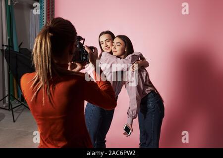 Bild von zwei Mädchen, die Umarmung und und von weiblichen Kameramann im Studio fotografiert werden Stockfoto