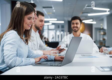 Menschen haben Business Konversation. Seitliche Sicht auf Mädchen arbeitet auf der silbernen Laptop im Büro und lächelnd Stockfoto