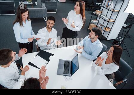 Mitarbeiter begrüßen. Blick von oben auf die Büroangestellten in der klassischen Verschleiß sitzen in der Nähe des Tisches mit Laptop und Dokumente Stockfoto