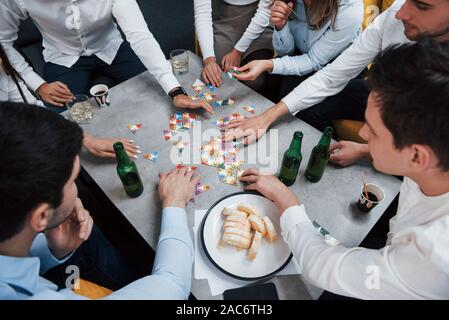 Ansicht von oben. Entspannen mit Spiel. Feiern erfolgreichen Abschluss. Junge Berufstätige sitzt in der Nähe des Tisches mit Alkohol Stockfoto