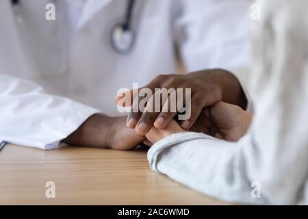 Junge Frau mit Händen der afrikanischen amerikanischen männlichen Arzt, Nahaufnahme. Stockfoto