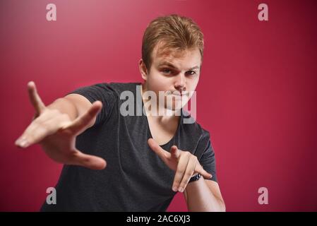 Junge pathos Teenager, junge, tragen, grau t-shirt über isolierte rosa Hintergrund tun Rock Symbol mit hands up. Musik Star. yo unterzeichnen. Cool anmelden Stockfoto