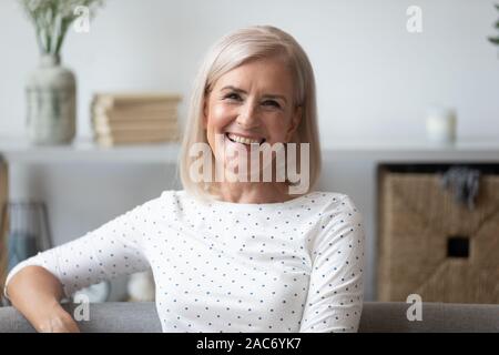 Headshot gealterte Frau lächelnd Sitzen auf der Couch bei Camera suchen Stockfoto