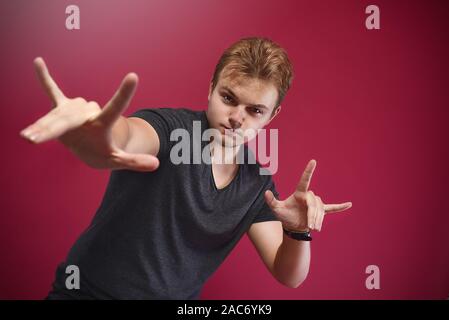 Junge pathos Teenager, junge, tragen, grau t-shirt über isolierte rosa Hintergrund tun Rock Symbol mit hands up. Musik Star. yo unterzeichnen. Cool anmelden Stockfoto