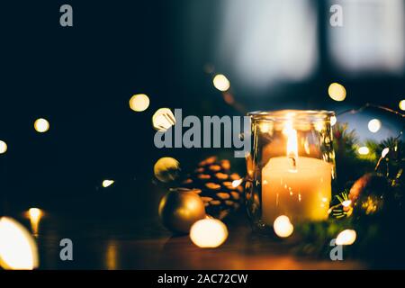 Weihnachten Kerze in einer recyceltem Glas Glas auf dem Tisch mit Tannenzweigen, Weihnachtsbeleuchtung und Ornamente. Home Fenster in den Hintergrund Stockfoto