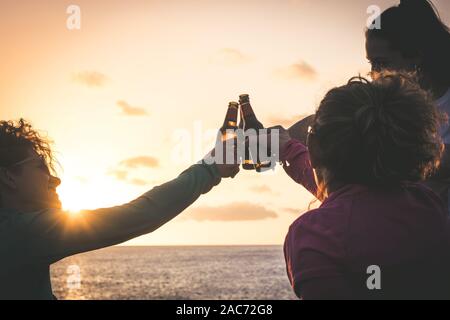 Grüße an die besten Freunde, Freunde genießen Getränke am Abend am Strand bei Sonnenuntergang. Hände, die Flaschen Bier halten. Konzept der Ferienhäuser, Pflege Stockfoto