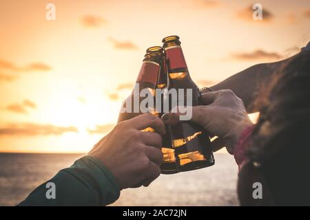 Grüße an die besten Freunde, Freunde genießen Getränke am Abend am Strand bei Sonnenuntergang. Hände, die Flaschen Bier halten. Konzept der Ferienhäuser, Pflege Stockfoto