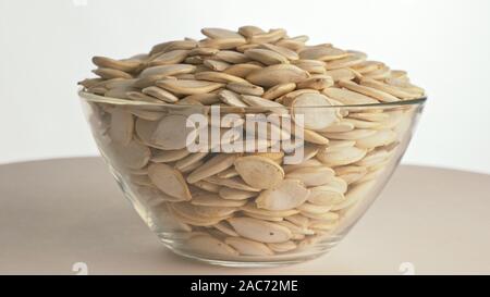 Muttern ungeschälte Kürbiskerne drehen sind auf eine Tabelle in einer Platte. Snack in durchsichtigen Teller auf einem isolierten weißen Hintergrund drehen sich bewegt. Lecker Stockfoto