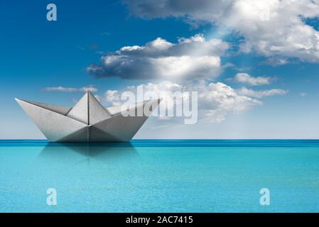 Weißbuch Boot, Origami, im türkisfarbenen Meer mit blauem Himmel, Wolken und Sonnenstrahlen. Stockfoto