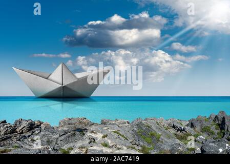 Weißbuch Boot, Origami, im türkisfarbenen Meer mit blauem Himmel, Wolken und Sonnenstrahlen. Stockfoto