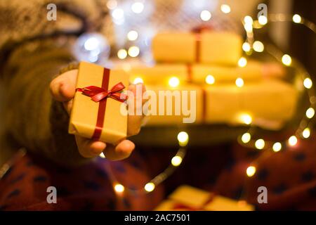 Hand hält sie eine Geschenkverpackung. Mädchen in einem gestrickten Pullover hält einen Stapel von geschenkboxen in einem braunen Handwerk Papier. Stockfoto