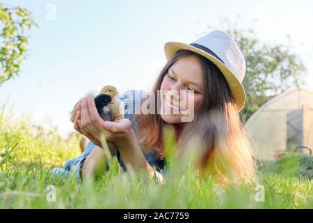 Outdoor Portrait von schönen lächelnden Teenager auf Bauernhof mit zwei neugeborene Küken in der Hand, Natur Hintergrund grün gras himmel Stockfoto