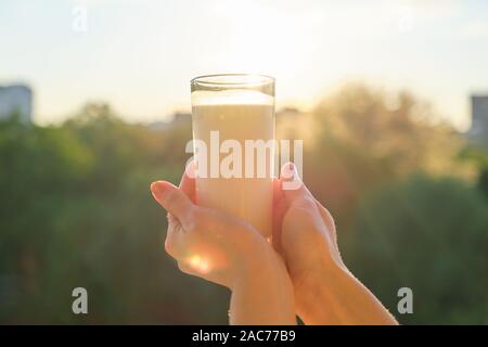 Glas mit Milch in womans Hand, Hintergrund, Sonnenuntergang, abend stadt Stockfoto