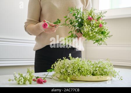 Frau florist mit unterschiedlichen Blumen auf dem Tisch, Bouquet, Blumen von Maiglöckchen, Rosen, viburnum. Floristik, Florist, f Stockfoto
