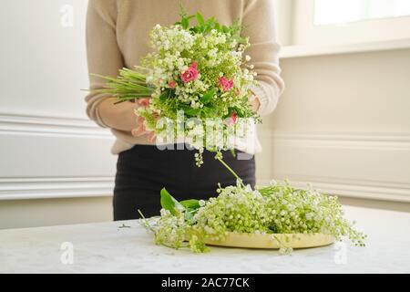 Frau florist mit unterschiedlichen Blumen auf dem Tisch, Bouquet, Blumen von Maiglöckchen, Rosen, viburnum. Floristik, Florist, f Stockfoto