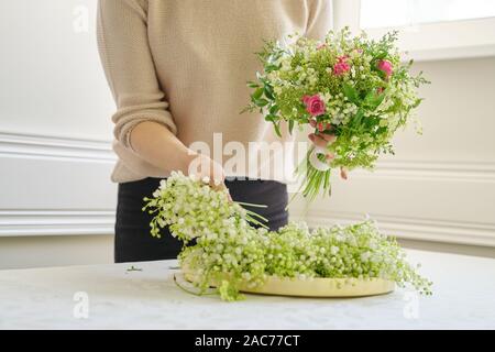 Frau florist mit unterschiedlichen Blumen auf dem Tisch, Bouquet, Blumen von Maiglöckchen, Rosen, viburnum. Floristik, Florist, f Stockfoto