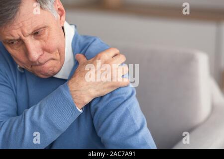 Senior Gentleman in Schmerzen Schulter sitzen auf der Couch Stockfoto