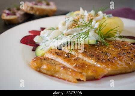 Essen Fotografie eines vegane Schnitzel, gekochte Kartoffeln und eine Dill und Joghurt Sauce auf einem schwarzen Schiefer Hintergrund und ein rotes Tuch Stockfoto