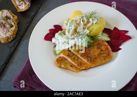 Essen Fotografie eines vegane Schnitzel, gekochte Kartoffeln und eine Dill und Joghurt Sauce auf einem schwarzen Schiefer Hintergrund und ein rotes Tuch Stockfoto