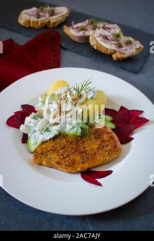 Essen Fotografie eines vegane Schnitzel, gekochte Kartoffeln und eine Dill und Joghurt Sauce auf einem schwarzen Schiefer Hintergrund und ein rotes Tuch Stockfoto