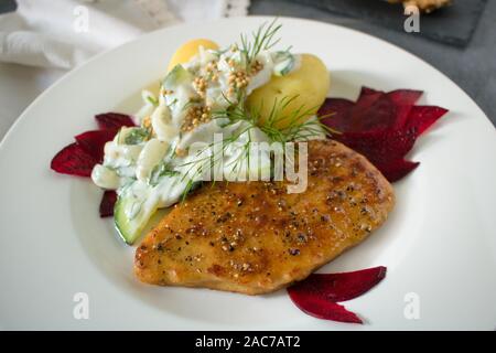 Essen Fotografie eines vegane Schnitzel, gekochte Kartoffeln und eine Dill und Joghurt Sauce auf einem schwarzen Schiefer Hintergrund und ein rotes Tuch Stockfoto