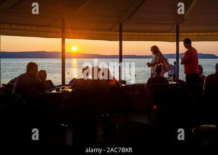 Die Gäste in einem Restaurant am Meer auf der Insel Cres beobachten Sie den Sonnenuntergang über die Kvarner Bucht, Kroatien Stockfoto