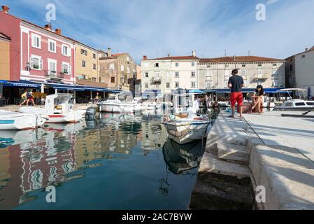 Junges Paar im Gespräch mit Fischer im Hafen der Altstadt von Cres mit Cafés und Restaurants in der Morgensonne, Cres, Kvarner Bucht, Kroatien Stockfoto