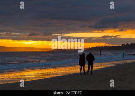 Bournemouth, Dorset UK. 1. Dezember 2019. UK Wetter: atemberaubende Sonnenuntergang am Strand von Bournemouth am Ende einer bitter kalt trockenen sonnigen Wintertag. Paar wandern entlang der Küste bei Sonnenuntergang. Credit: Carolyn Jenkins/Alamy leben Nachrichten Stockfoto