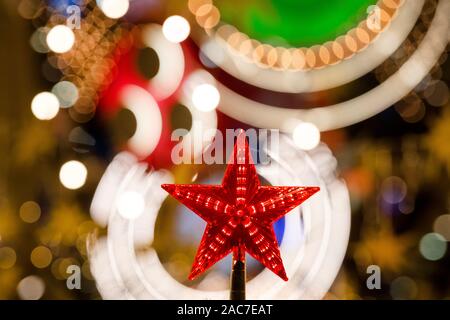Nahaufnahme von einem roten Stern am Weihnachtsbaum auf dem Hintergrund der festliche Lichter in der Nacht die Stadt für das Neue Jahr Stockfoto